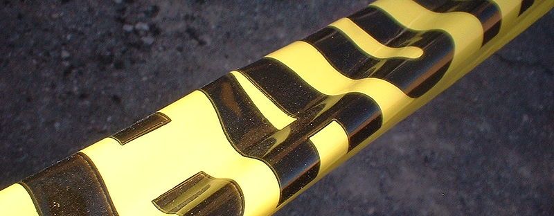 Yellow caution tape in close up crosses diagonally from lower left to upper right over a blurry dark background of rubble or asphalt